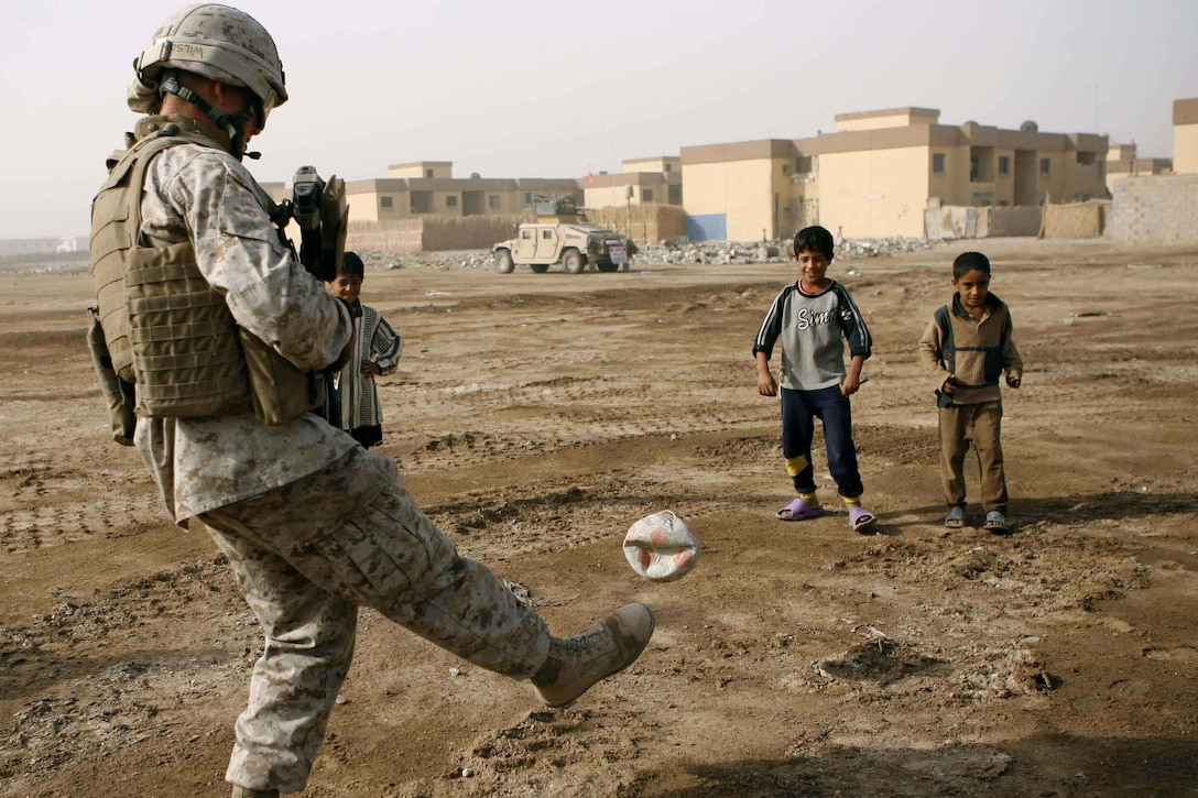 A man in a military uniform kicks a deflated ball to two children.