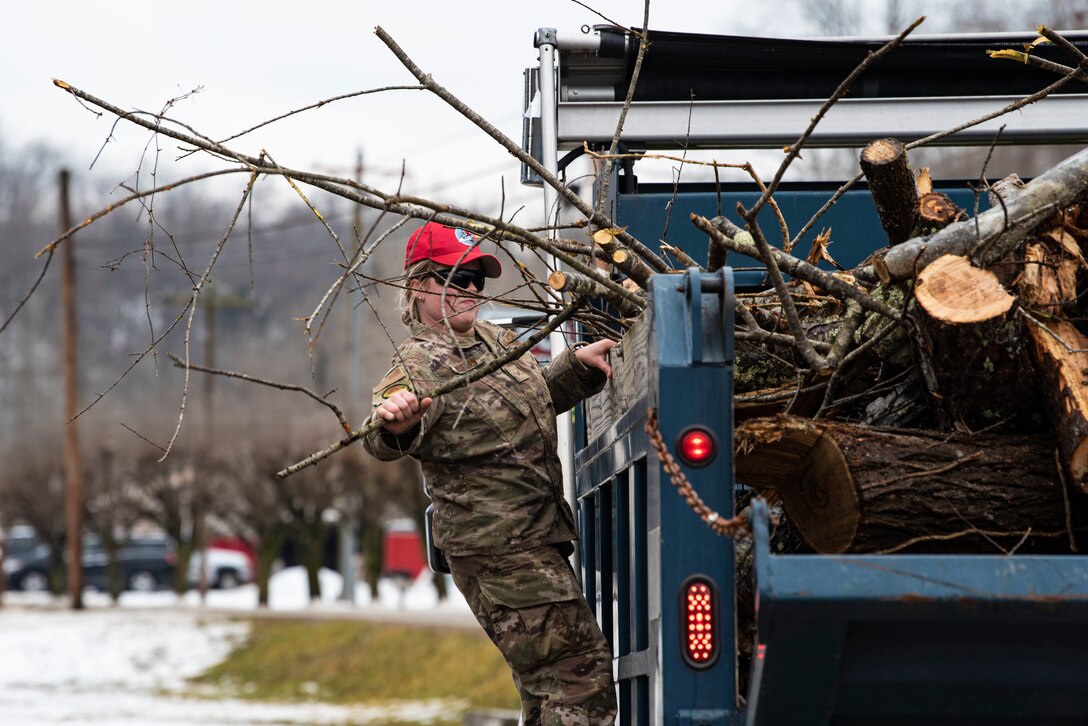 An airman adjusts tree debris in the back of a vehicle.