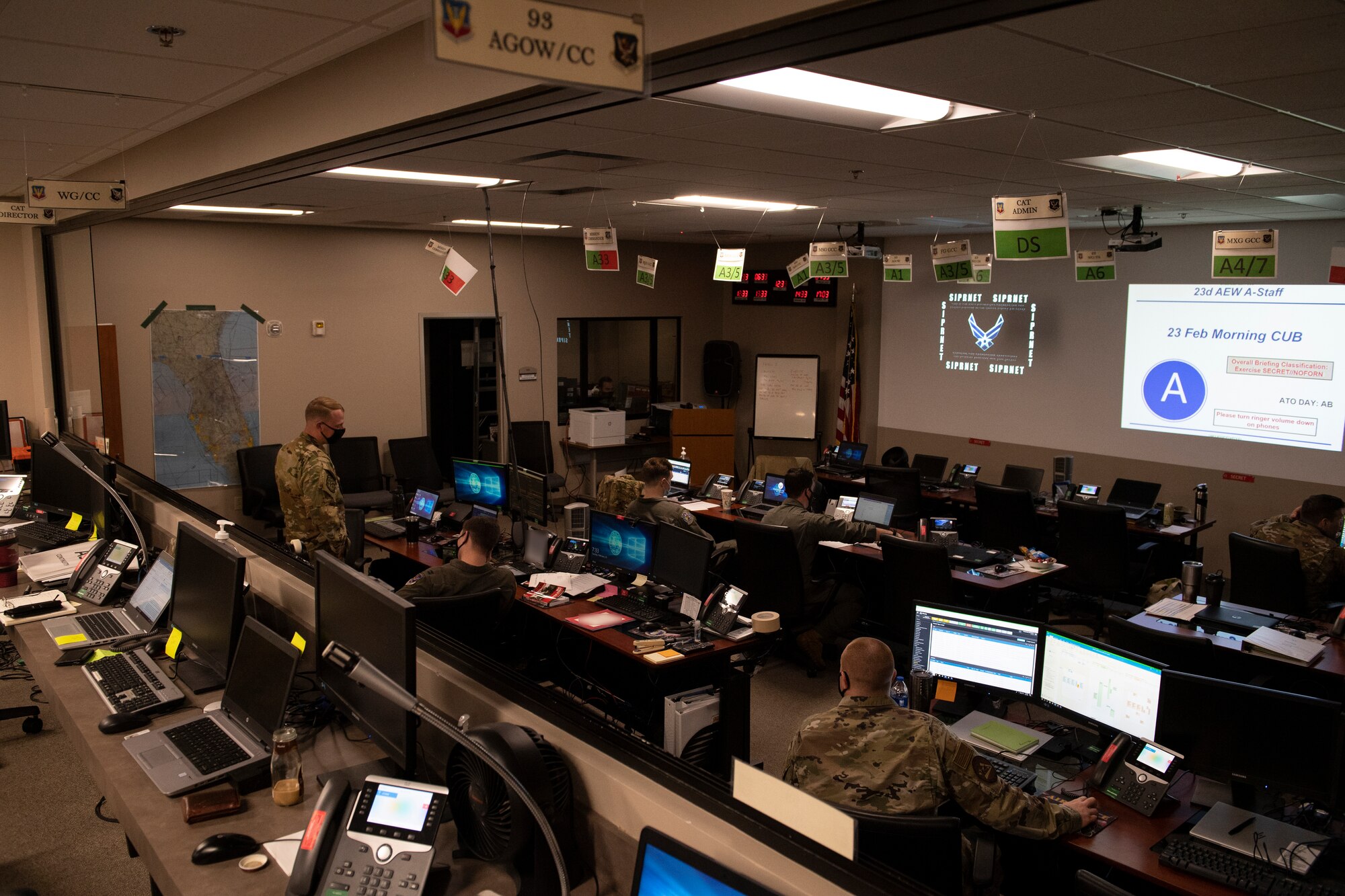 A photo of a room full of computers and people standing and sitting.