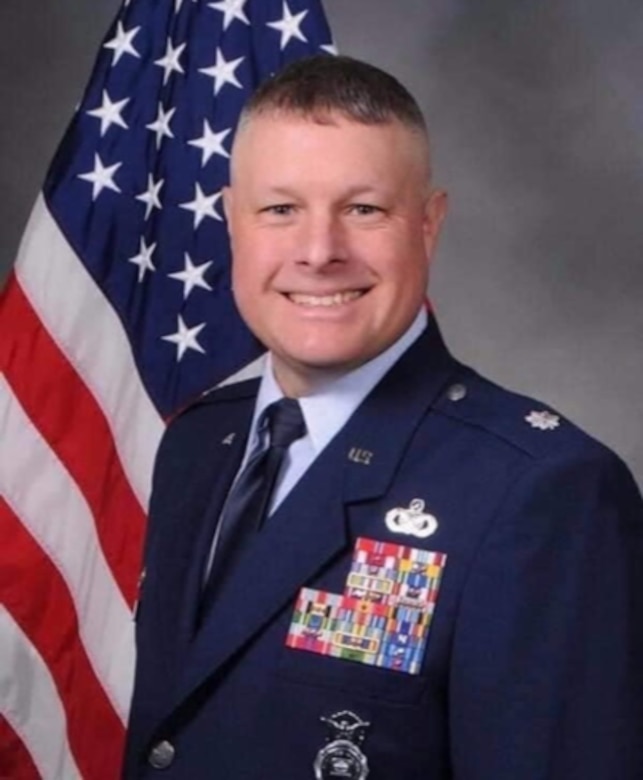 Air Force officer in official photograph with an American flag in the background.