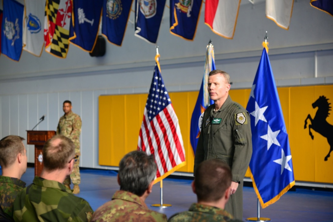 A man in a military flight suit speaks to service members.