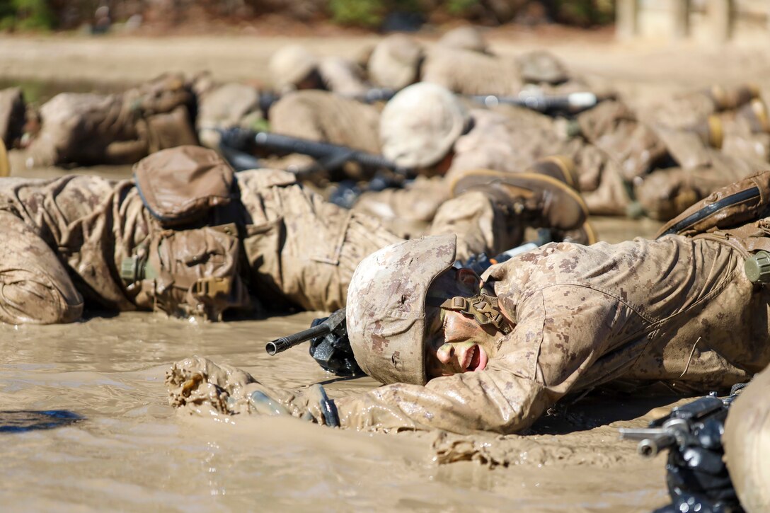 A group of recruits crawl in mud.
