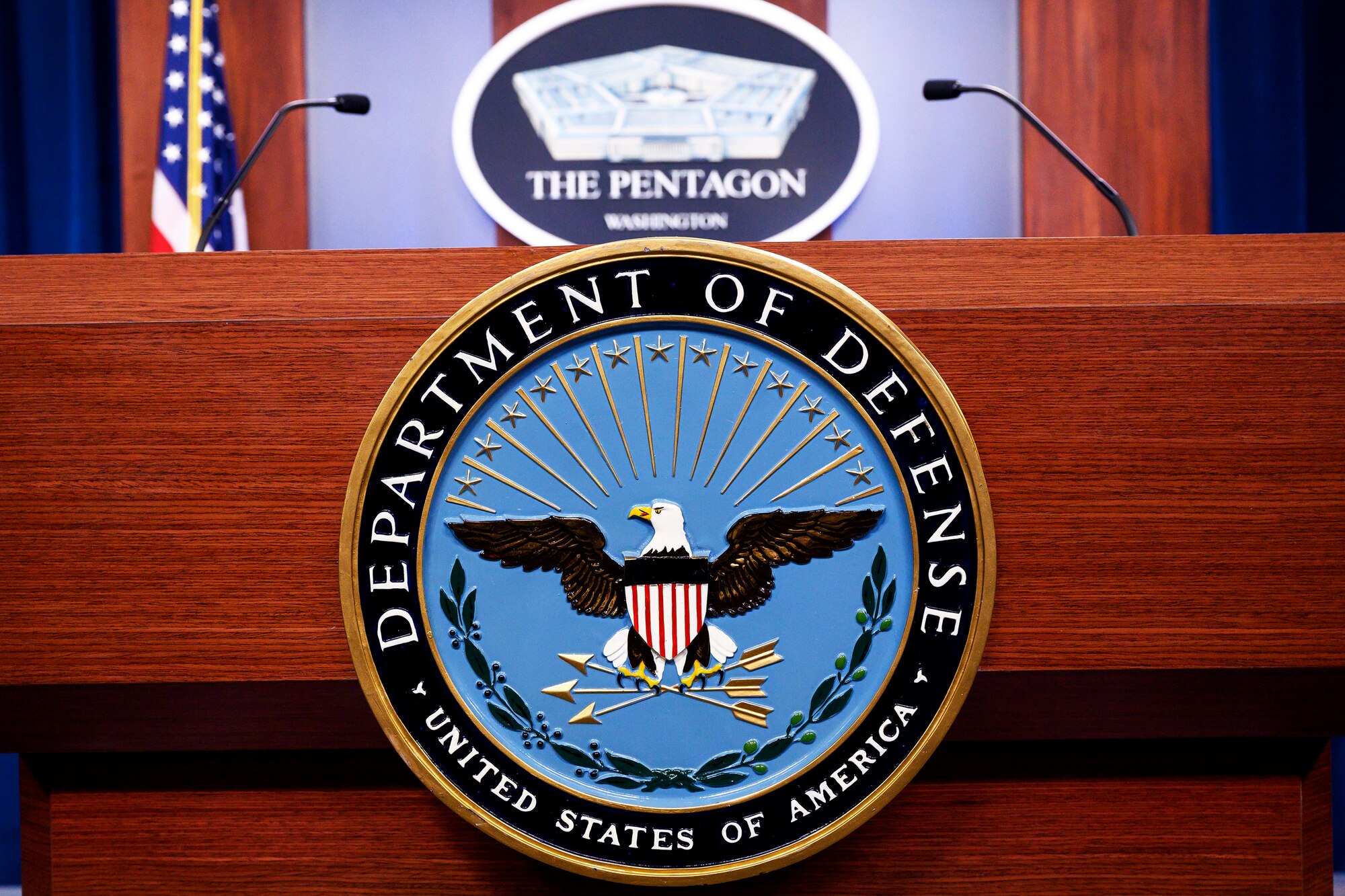 The Defense Department seal adorns a lectern where two microphones stand.