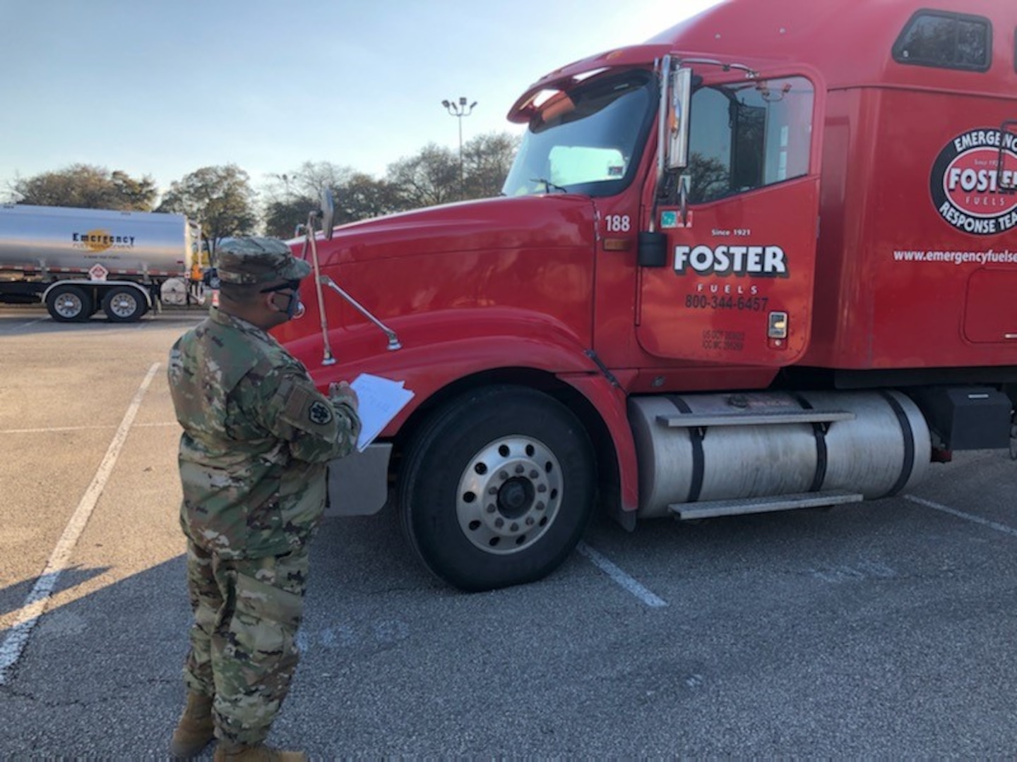 A man in military uniform looks at a big fuel truck