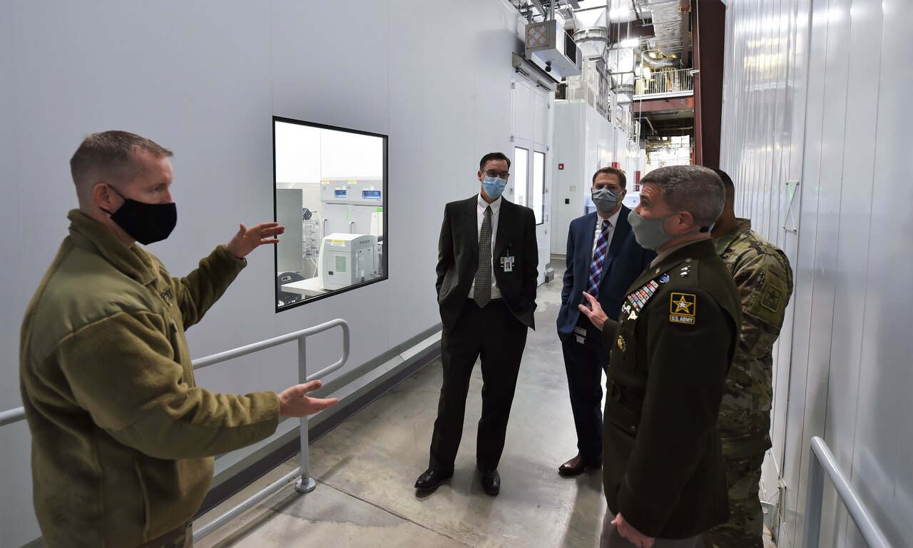 Army leaders wearing face masks discuss operations at a biotechnology facility.