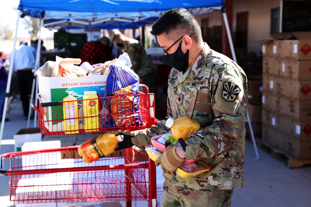 A guardsman wearing a face mask and gloves carries groceries and puts them in a cart that will be distributed to local citizens.