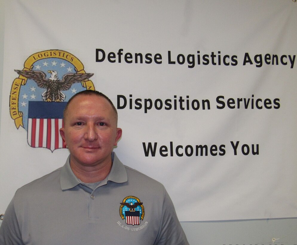 Man in grey DLA logo polo stands in front of a white DLA welcome sign