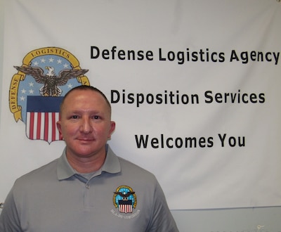 Man in grey DLA logo polo stands in front of a white DLA welcome sign