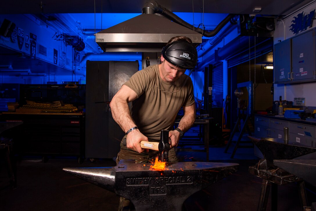 An airman shapes a piece of hot steel into a knife.