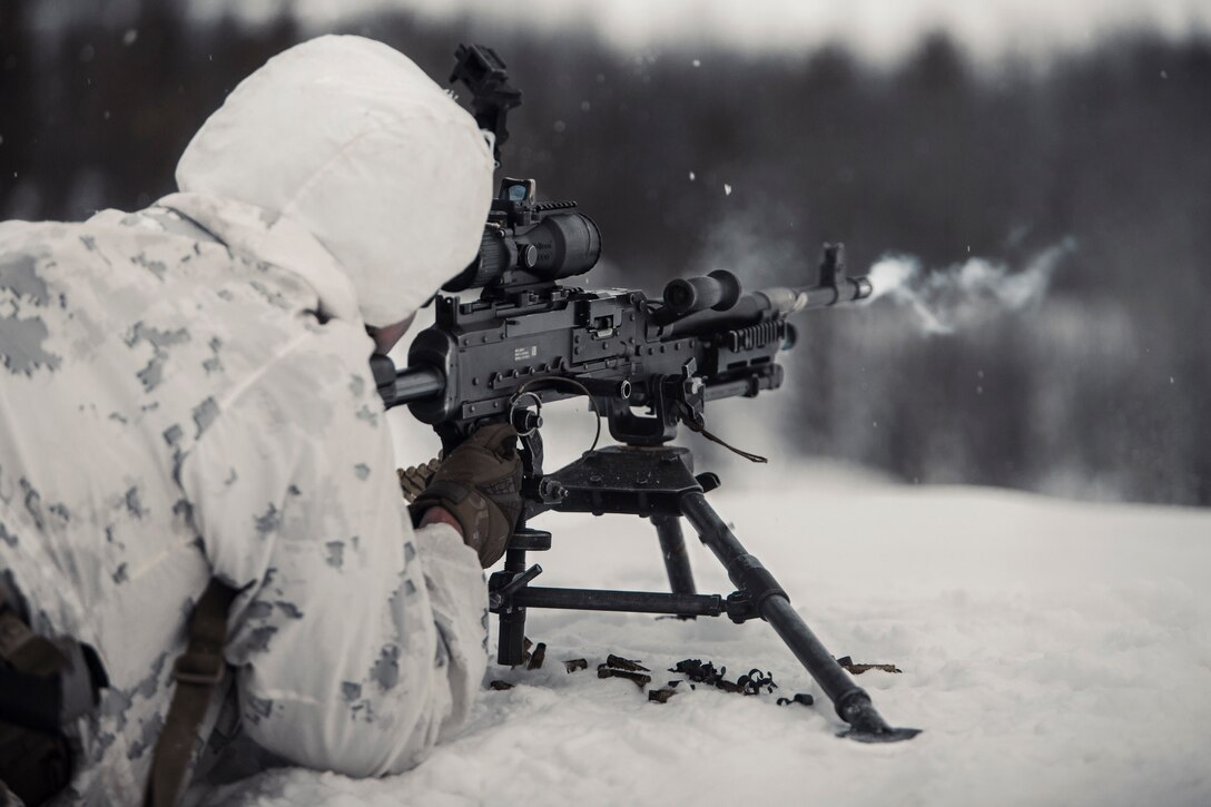 A Marine fires a weapon while lying in the snow.