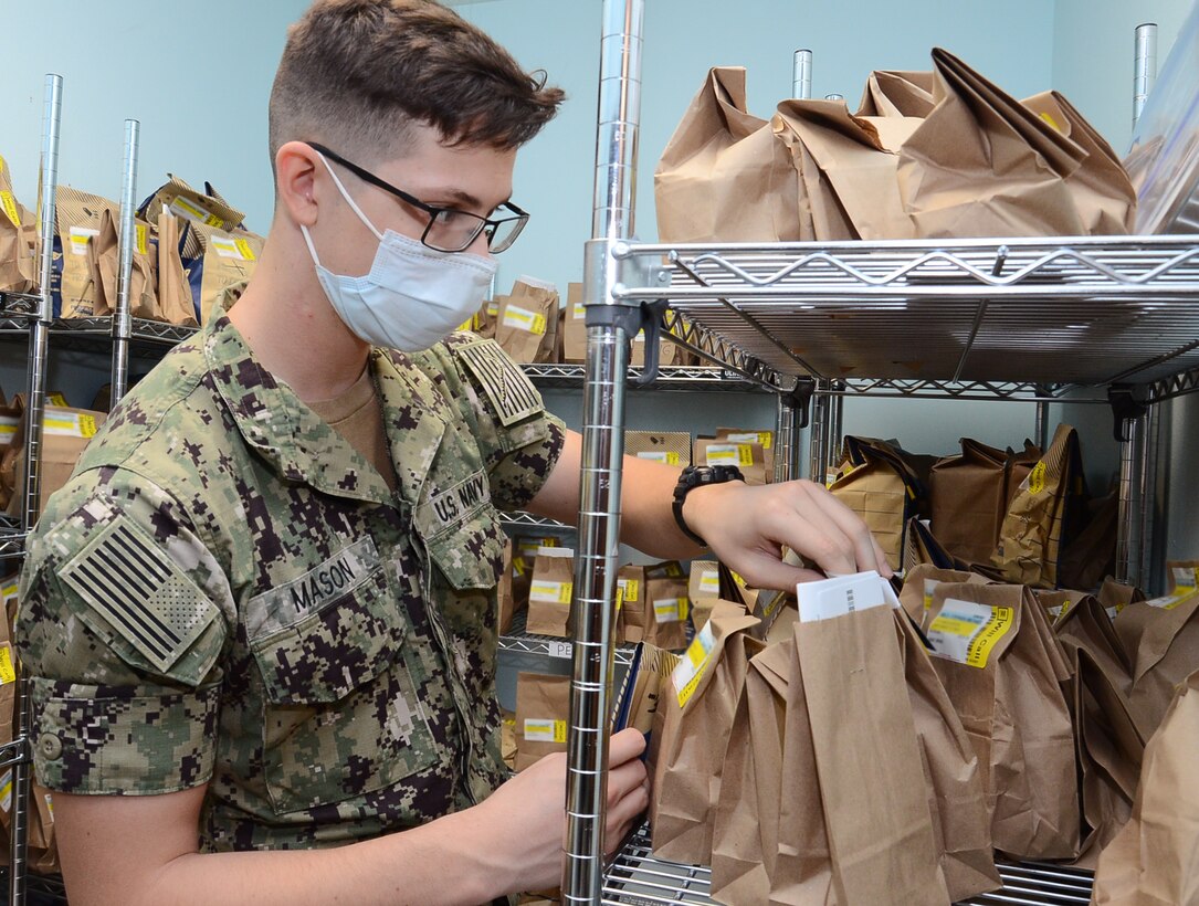 A sailor wearing a face mask fills prescriptions