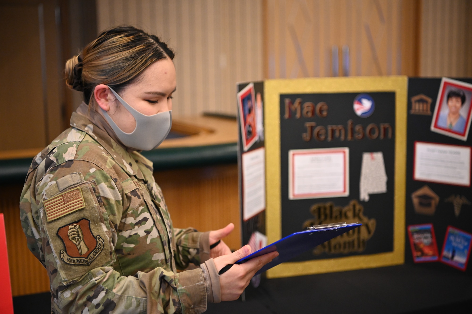 Women in uniform looks at notebook while presenting a display.