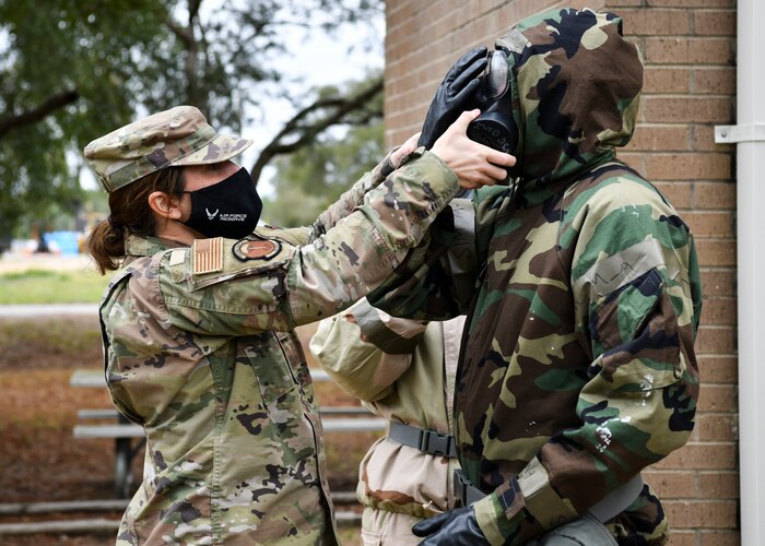An instructor pulls on the vents of a gas mask an Airman in full protective gear is wearing.