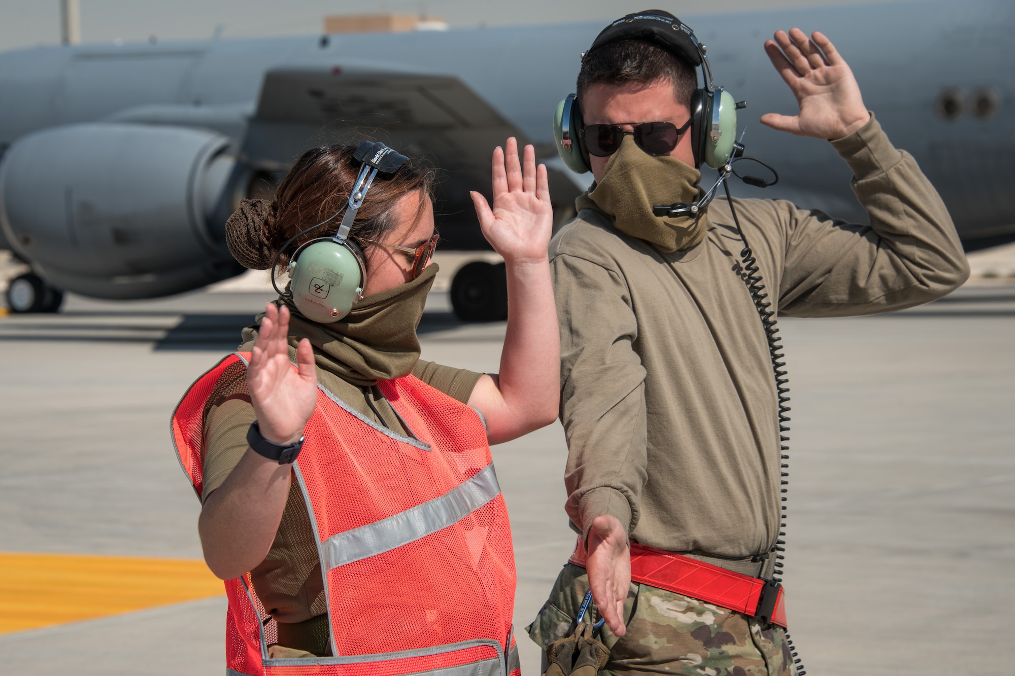 Two airmen use their arms to signal an aircraft pilot who is out of frame