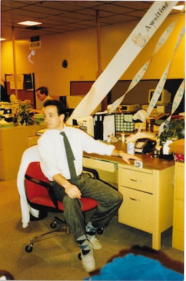 A young Michael Scott is seated at his desk in a late 1980's to early 1990's office setting.