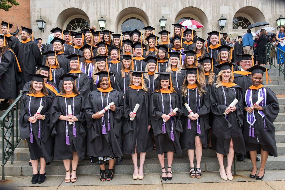 A large group of people wearing graduation caps and gowns pose for a photo on steps.