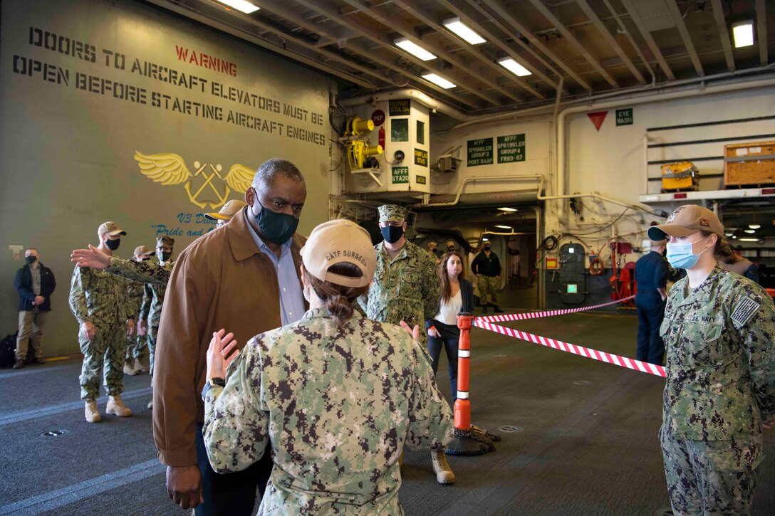 Secretary of Defense Lloyd J. Austin III speaks to a service member; others stand around.