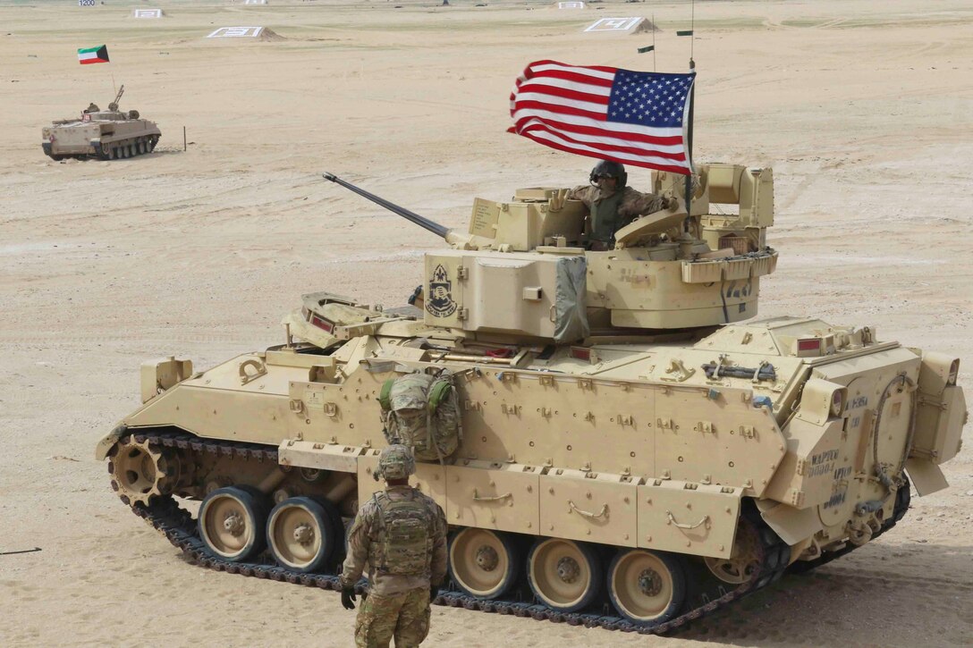 A soldier inside a tank talks to another soldier standing outside.