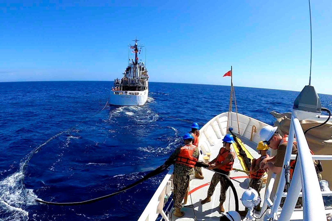 Coast Guardsmen stand on the deck of a ship as another ship sails in front.