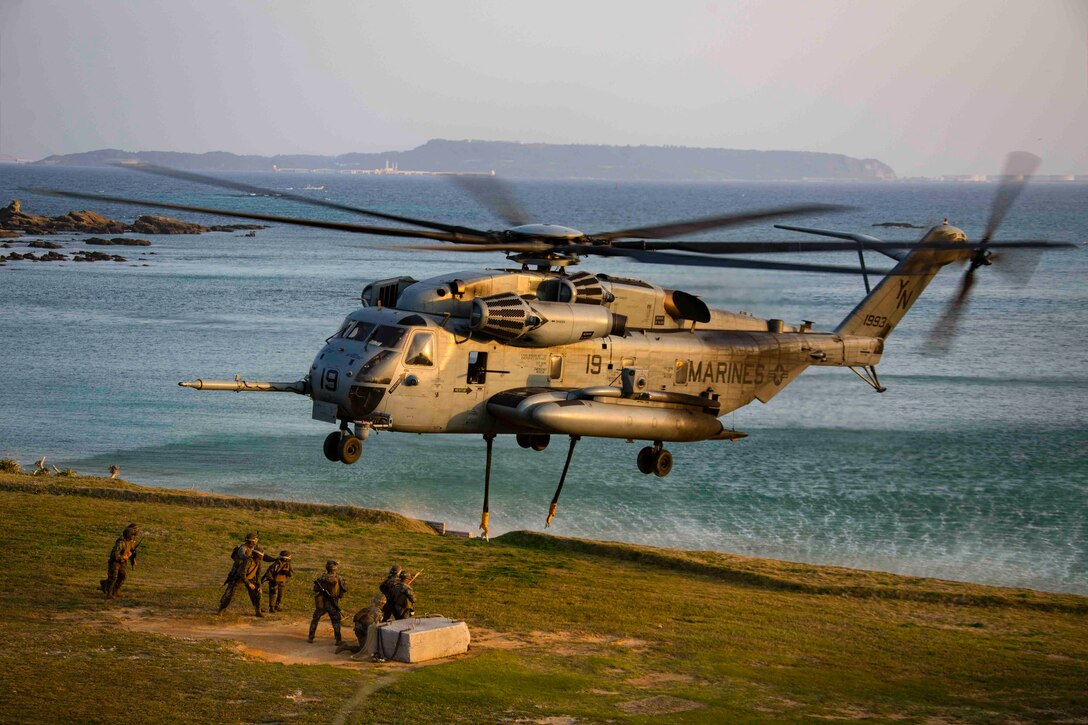 Marines stand beneath an airborne helicopter.