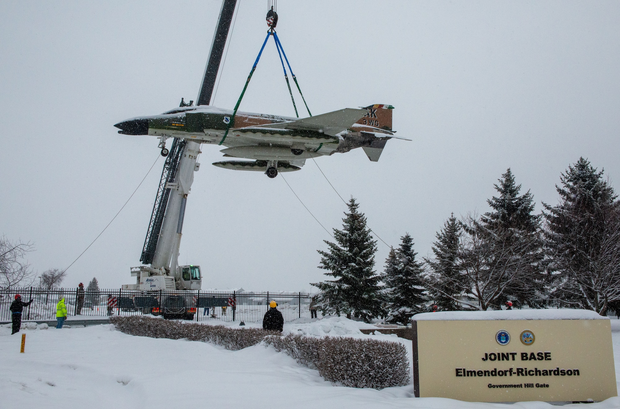 Members from the 3rd Maintenance Squadron assigned to the 3rd Wing, and Alaska Crane civilian contractors hoist the McDonnell F-4C Phantom II static display in front of the Government Hill Gate at Joint Base Elmendorf-Richardson, Alaska, Feb 18, 2021.