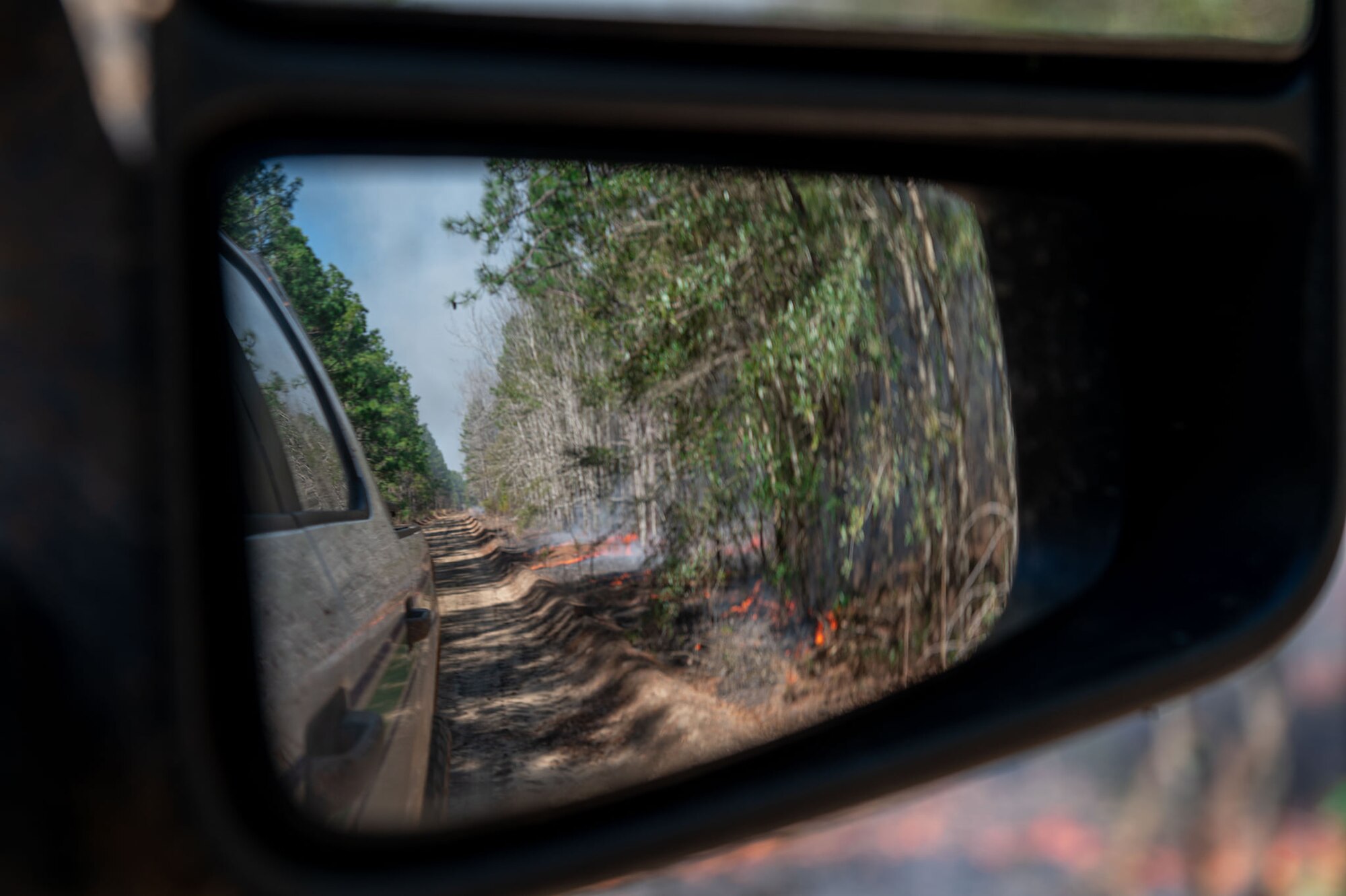 A photo of a sideview mirror with a fire reflected in it.