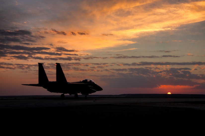A fighter aircraft is seen on the ground against the setting sun.
