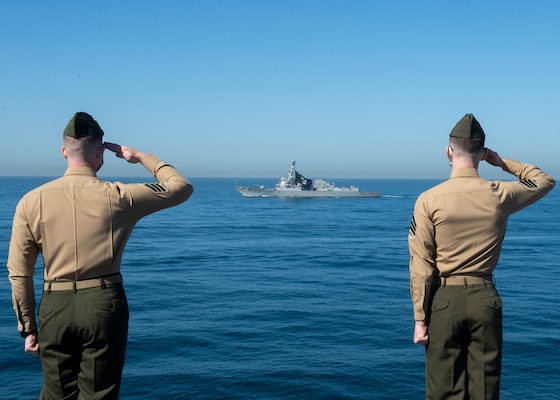 United States Marines render honors to the Arleigh Burke-class destroyer USS Michael Murphy (DDG 112) from the flight deck of the aircraft carrier USS Nimitz (CVN 68).