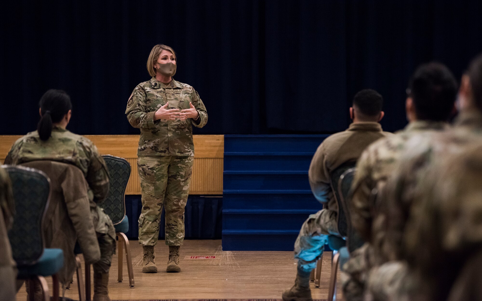 Woman in uniform talks on stage in front of military members