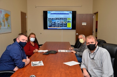 Four people sit around a conference tale looking towards the camera. Each person is wearing a mask.