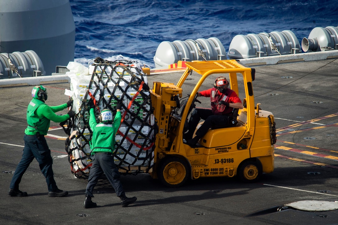 Sailors move a pallet on a ship.