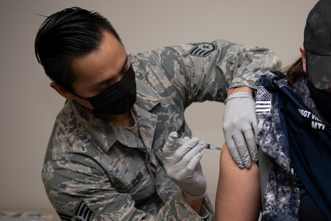 An airman administers a vaccine to another airman.