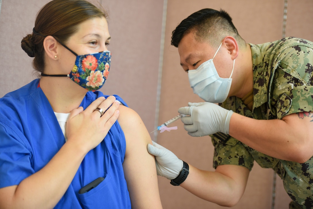 A sailor wearing a mask inoculates a woman wearing a mask.