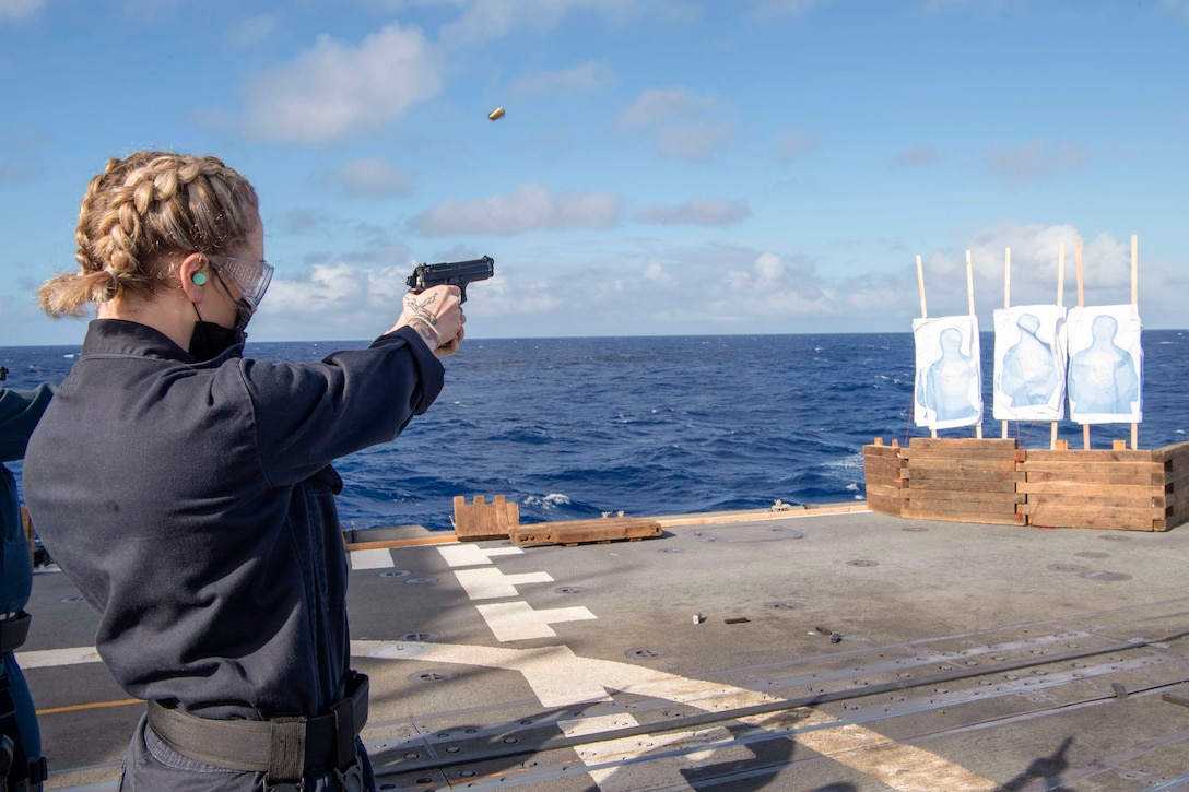 A sailor fires a weapon on a ship during training.