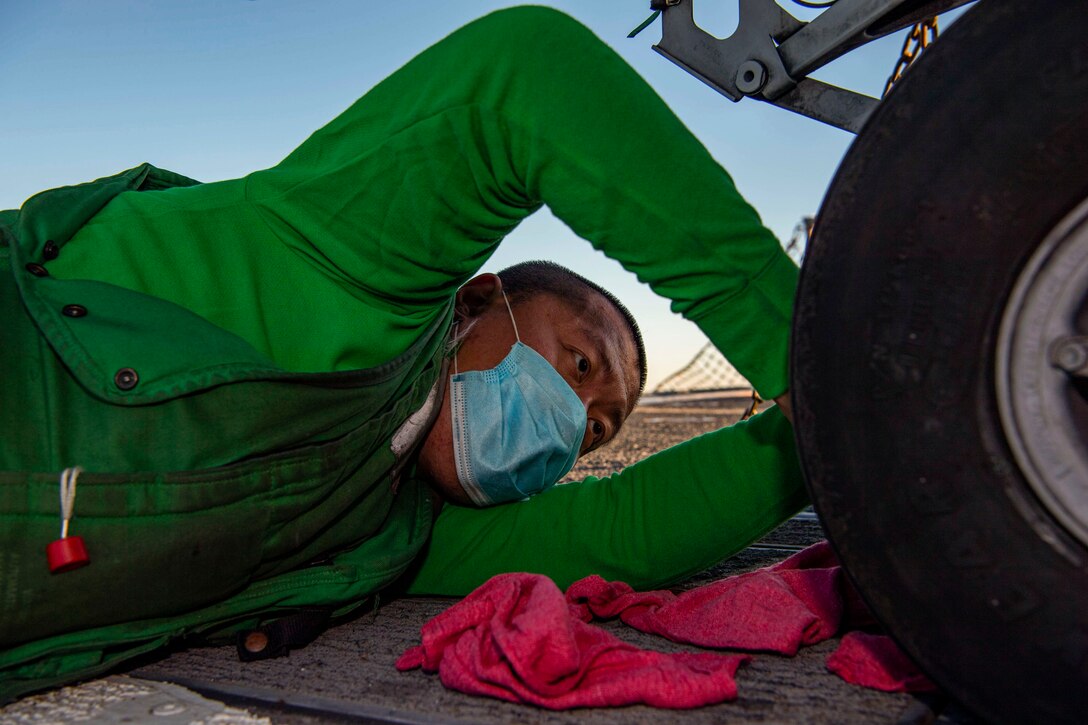 : A sailor wearing a mask works on a helicopter’s wheel.