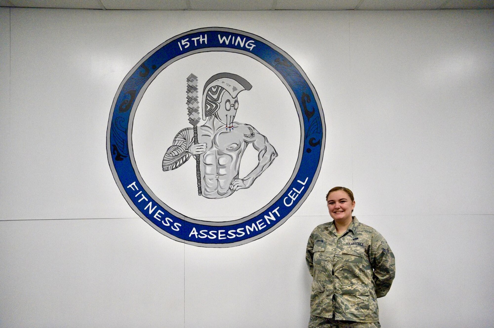 Airman 1st Class Tessa Hanson, 647th Force Support Squadron services journeyman, presents her finished painting project at the Fitness Assessment Cell at Joint Base Pearl Harbor-Hickam, Hawaii, Dec. 12, 2020. Hanson completed a series of paintings at the FAC with the purpose of motivating Airmen testing during their physical fitness assessment. (Air Force photo by 2nd Lt Benjamin Aronson)