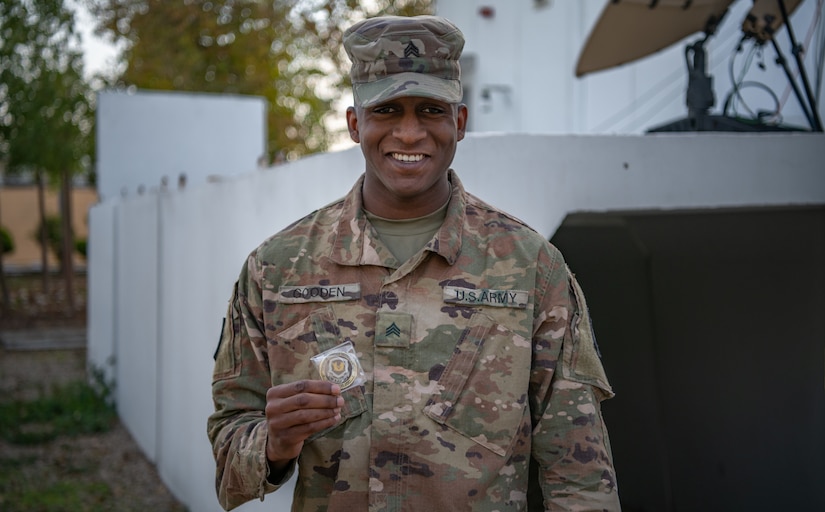 Sgt. Kha'lee Gooden, the National Security Law Paralegal Non-commissioned officer assigned to the 75th Field Artillery Brigade, the “Diamond Brigade”, of Fort Sill, OK, poses with a coin he had just received from Col. Tonya Blackwell, the Staff Judge Advocate for the Fires Center of Excellence and Fort Sill, while deployed to the Middle East in support of Operation Spartan Shield and Operation Inherent Resolve, December 15, 2020. Sgt. Gooden has continued to demonstrate outstanding leadership both within and outside of the Diamond Brigade. (U.S. Army photo by Sgt. Dustin D. Biven / 75th Field Artillery Brigade)