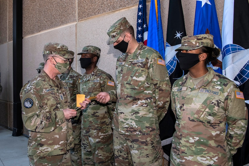 Man in a military uniform hands service identification tapes to new Space Force guardians.