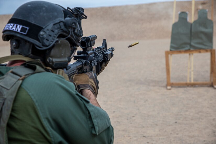 A bullet leaves a gun as a marine shoots a rifle at a range.