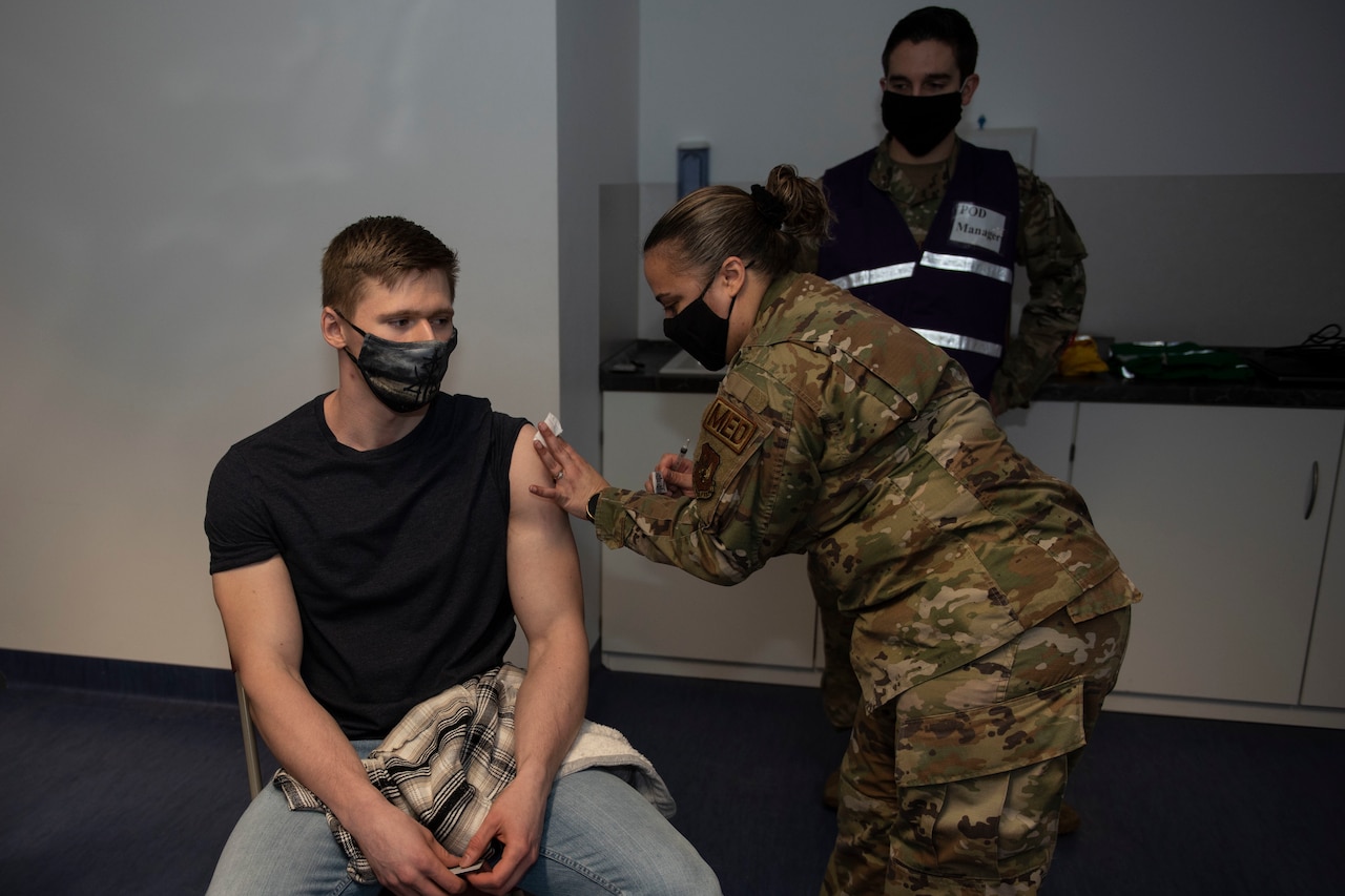 An airman receives a vaccination from another airman.