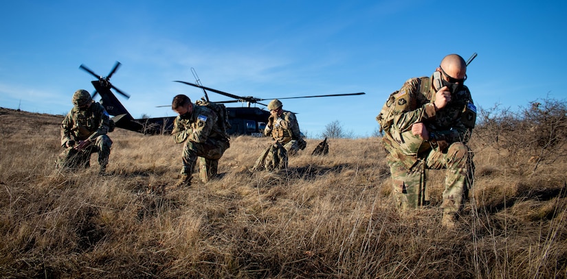 Soldiers kneel near a helicopter in a field.