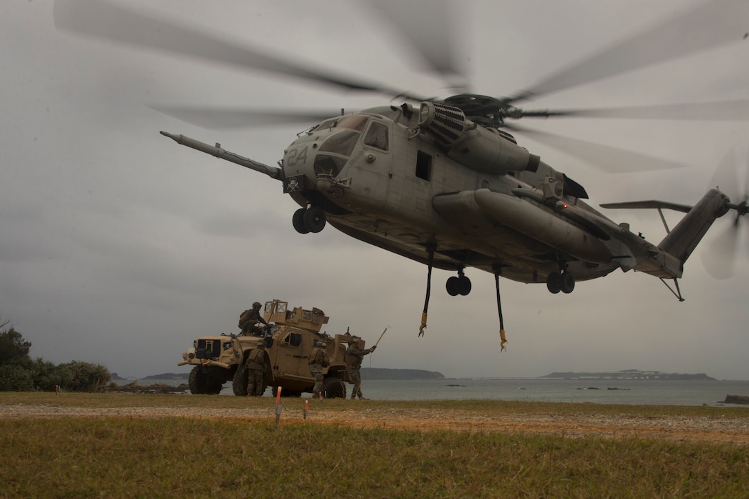 Marines prepare to attach a vehicle to an aircraft in a field.