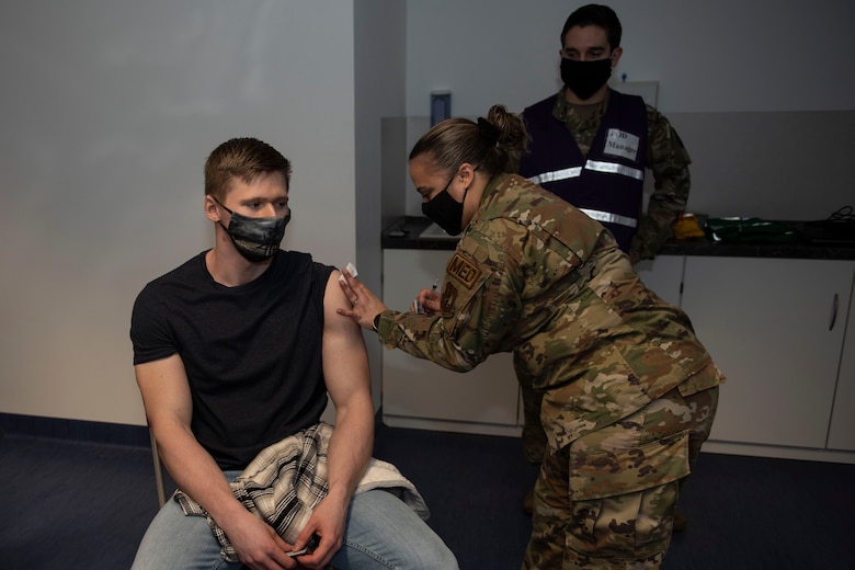 U.S. Air Force Senior Airman Brandon Franklin, 52nd Civil Engineer Squadron Fire and Emergency Services firefighter, receives the COVID-19 vaccine from Tech Sgt. Valeria Feist, 52nd Medical Operations Squadron allergy and immunization technician, Jan. 4, 2021, at Spangdahlem Air Base, Germany. Capt. Matthew Jordan, 52nd Medical Support Squadron chief of pharmacy operations, back, oversaw and hosted the first distribution of COVID-19 vaccinations for 52nd Fighter Wing Airmen, and ensured the process and comfort of service members were a priority. (U.S Air Force photo by Senior Airman Melody W. Howley)