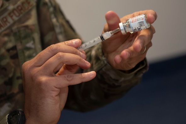 U.S. Air Force Senior Airman Brandon Franklin, 52nd Civil Engineer Squadron Fire and Emergency Services firefighter, receives the COVID-19 vaccine from Tech Sgt. Valeria Feist, 52nd Medical Operations Squadron allergy and immunization technician, Jan. 4, 2021, at Spangdahlem Air Base, Germany. Capt. Matthew Jordan, 52nd Medical Support Squadron chief of pharmacy operations, back, oversaw and hosted the first distribution of COVID-19 vaccinations for 52nd Fighter Wing Airmen, and ensured the process and comfort of service members were a priority. (U.S Air Force photo by Senior Airman Melody W. Howley)