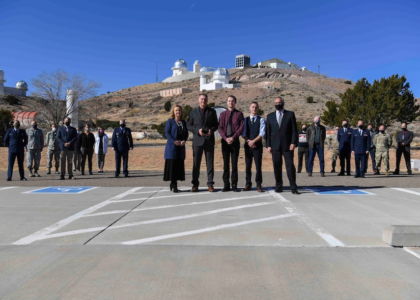 Service members and civilians stand for a photo in a parking lot.