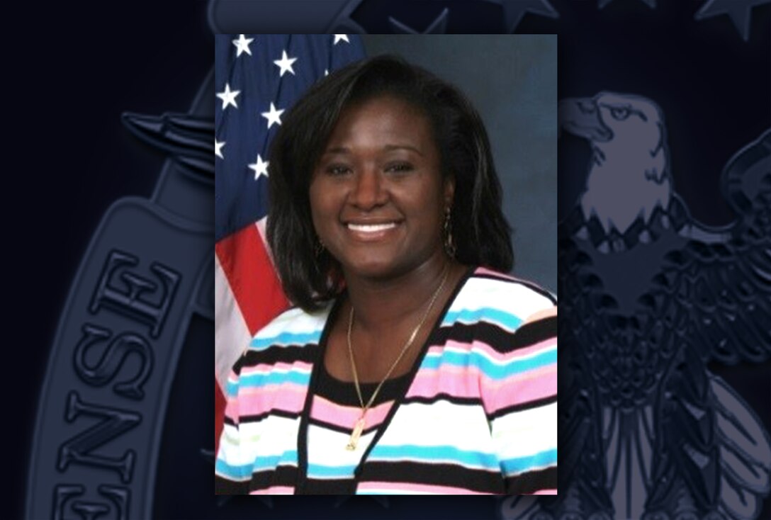 Head and shoulders image of a black woman wearing a black, white, pink and blue striped sweater posing in front of the US flag.