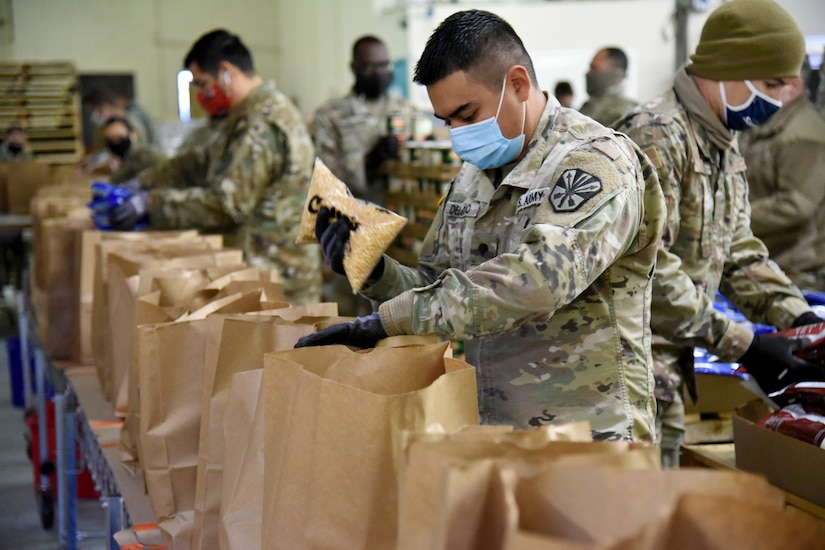 Service members fill paper bags with groceries.