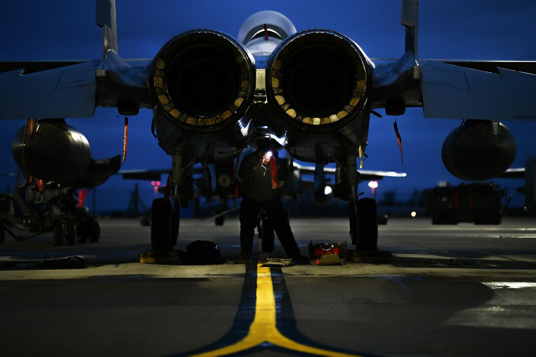 An airman looks at the underside of an aircraft.