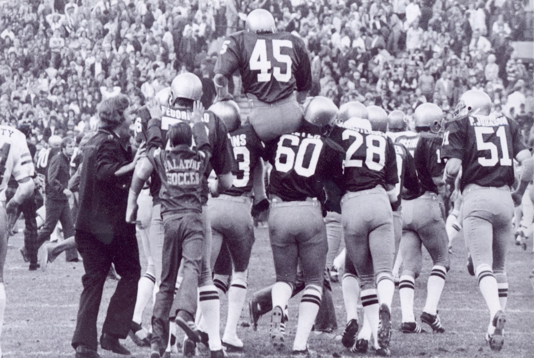 A line of football players carries another player on their shoulders off the field.