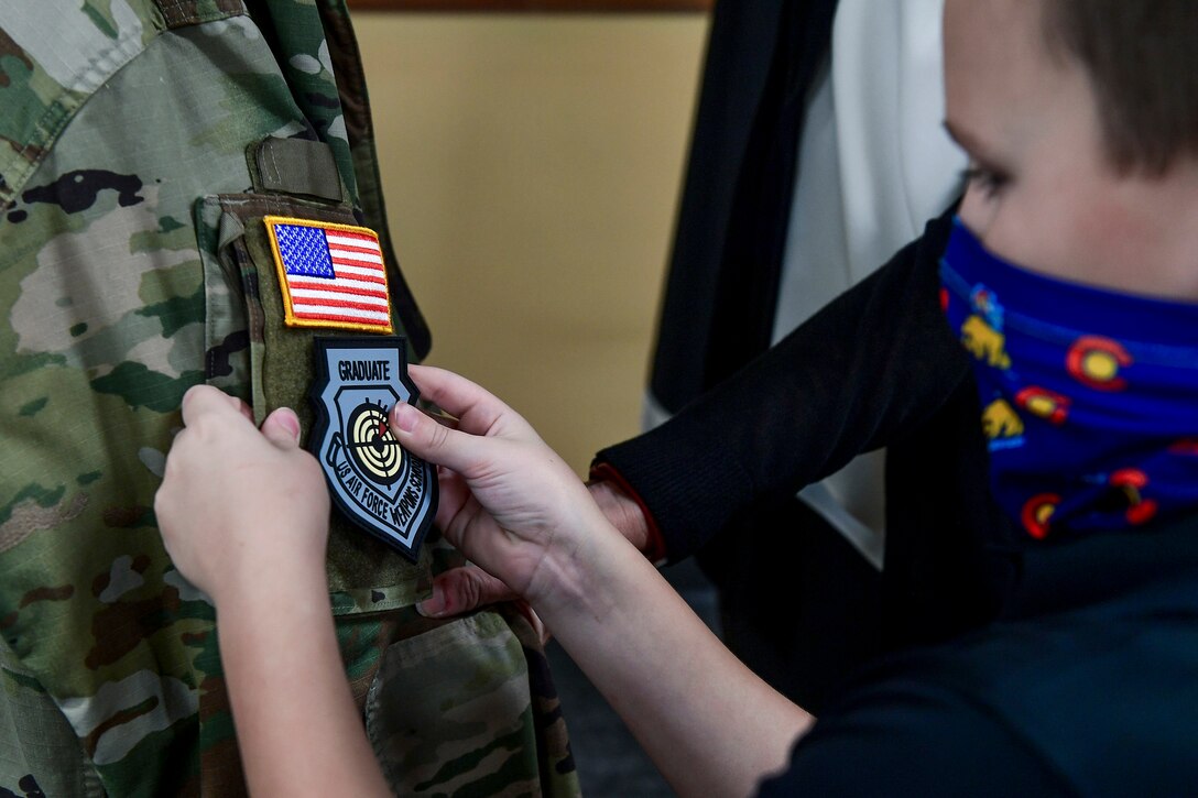 A child places a patch on the sleeve of his father's uniform.